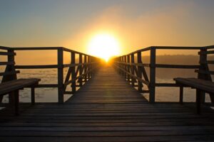 A dock over the ocean with a setting sun in the background.